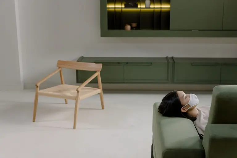 Asian woman wearing a face mask lying on a green couch, evoking calm and relaxation.