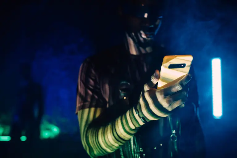 A person with futuristic makeup using a smartphone in a cyberpunk setting.