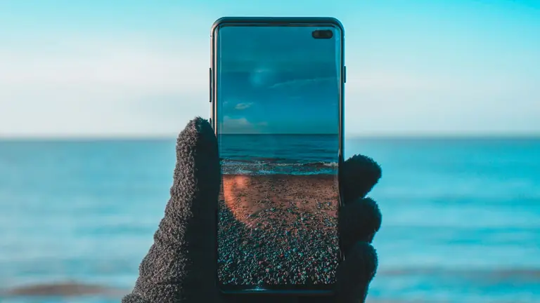 Smartphone displaying beach and ocean view on screen at sunset.
