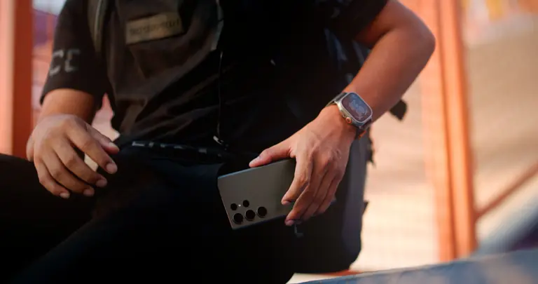 Casually dressed man with smartphone and smartwatch sitting outdoors, focusing on technology.