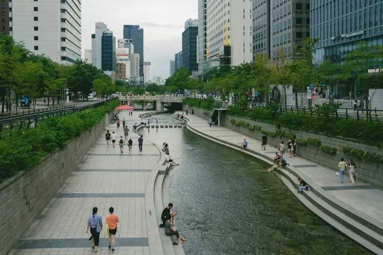a group of people walking along a river next to tall buildings