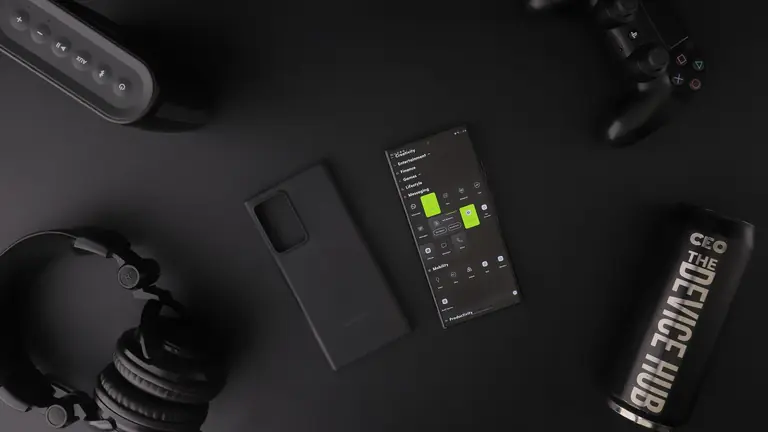 Overhead view of black modern electronics including smartphone, headphones, speaker, and controller on a table.