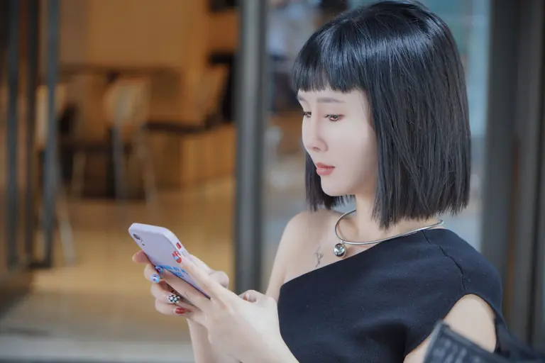 Asian woman in stylish attire using a smartphone indoors.