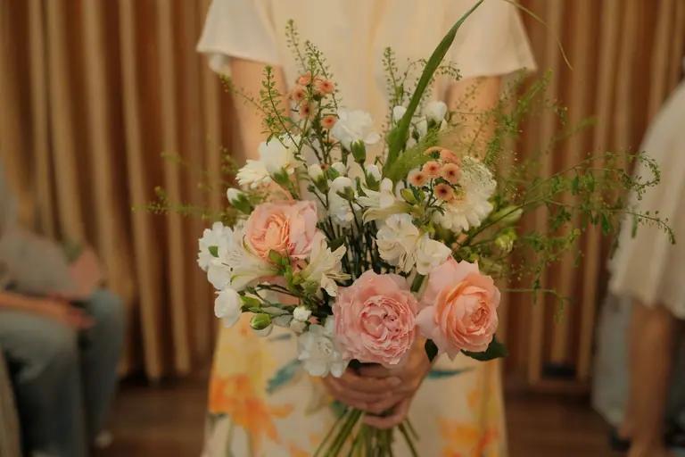 A beautiful floral bouquet held by a woman indoors.