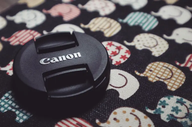 Canon lens cap on whimsical fabric with colorful elephant designs, perfect for creative photography themes.