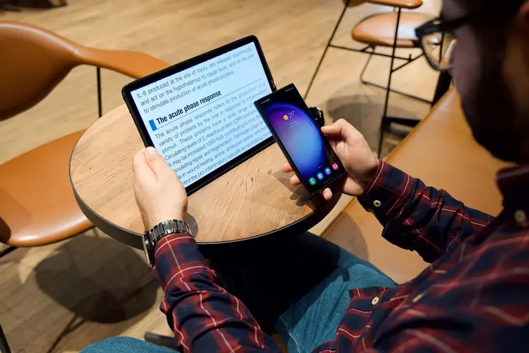A man using a tablet and smartphone at a coffee table in a modern indoor setting.