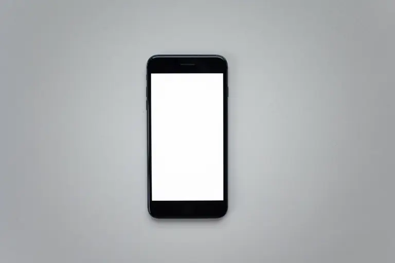 Top view of a black smartphone with a blank white screen on a gray surface.