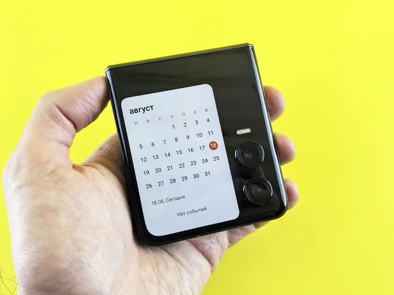 Close-up of a hand holding a flip smartphone with a calendar on screen against a vibrant yellow background.